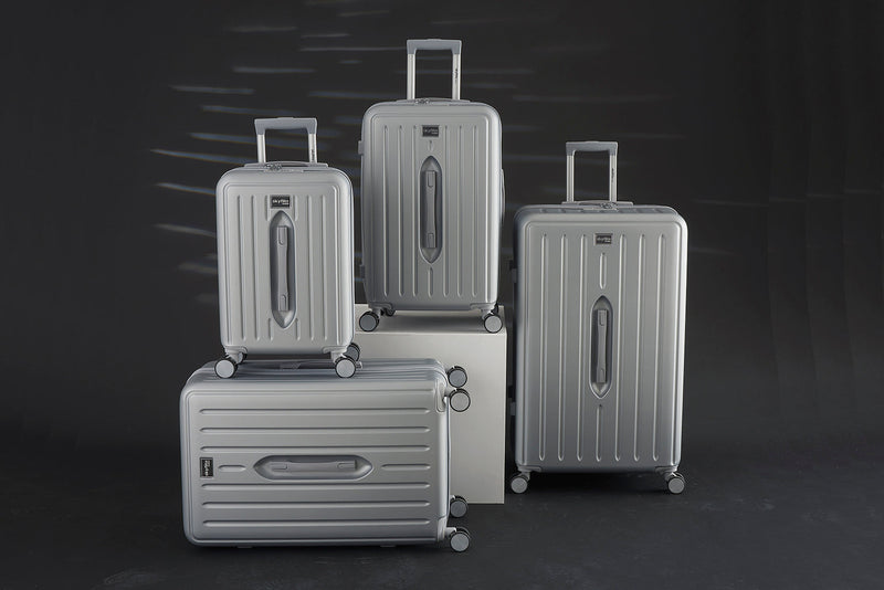 Four silver hard shell suitcases of different sizes with spinner wheels and telescopic handles, displayed against a dark background. The luggage features a modern, sleek design with vertical ridges and Skyflite branding.